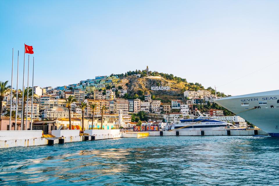 Cruise ship and ferry docked at Kusadasi port beneath a hillside sign